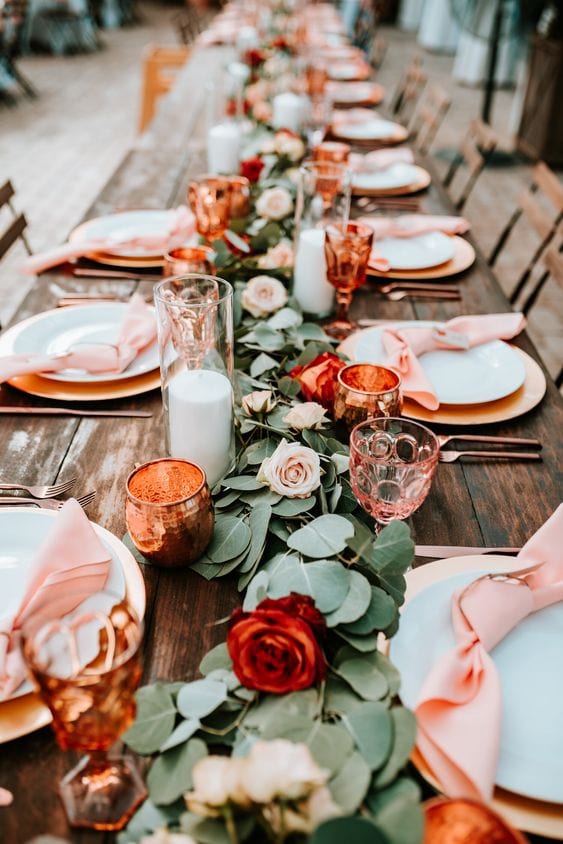 Green trestle laid along the centre of a table with few and far between red roses and terracotta bud vases make for a fun wedding theme.