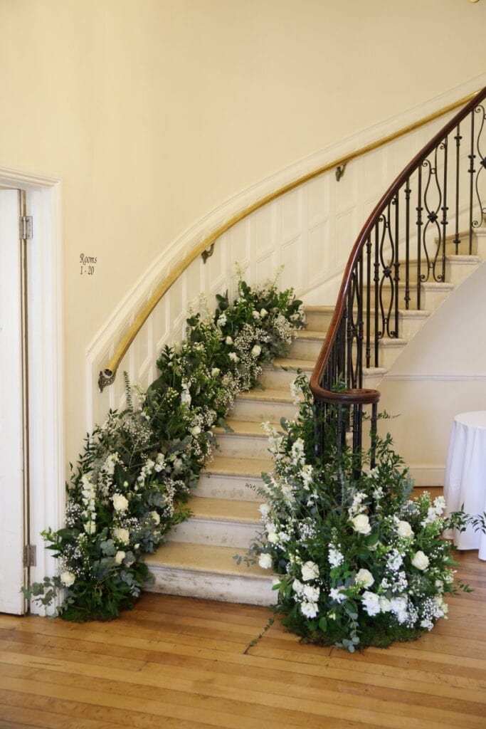 All classic whites are another top winter wedding trend. Here, green foliage creeps up a staircase with white and ivory flowers.